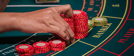 Eine Hand platziert Chips auf einem Baccarat Tisch.