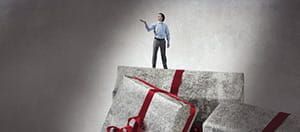 Ein Mann steht auf drei überdimensionierten Geschenkpaketen.