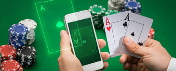 Hände vor einem Pokertisch mit Chips. In der linken Hand ein Smartphone und in der rechten Hand zwei Asse.