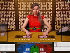 Das Bild zeigt einen Baccarat Tisch an dem eine blonde Dealerin gerade die Karten gegeben hat.