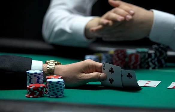 Ein Spieler schaut sich seine Karten an.  Gegenüber am Tisch sind die Hände eines Mitspielers.