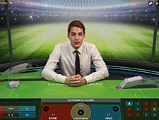 Das Bild zeigt ein Fußballstadion mit Kommentator vor einem grünen Spieltisch.